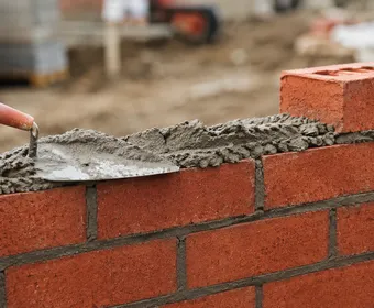 A bricklayer's trowel smoothing mortar along a new brick wall
