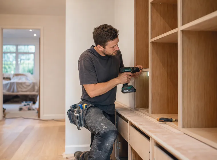 A joiner drilling into a bespoke built-in wooden wardrobe and shelving unit