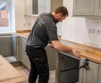 A joiner fitting a solid wood kitchen worktop, clamped in place while it's levelled